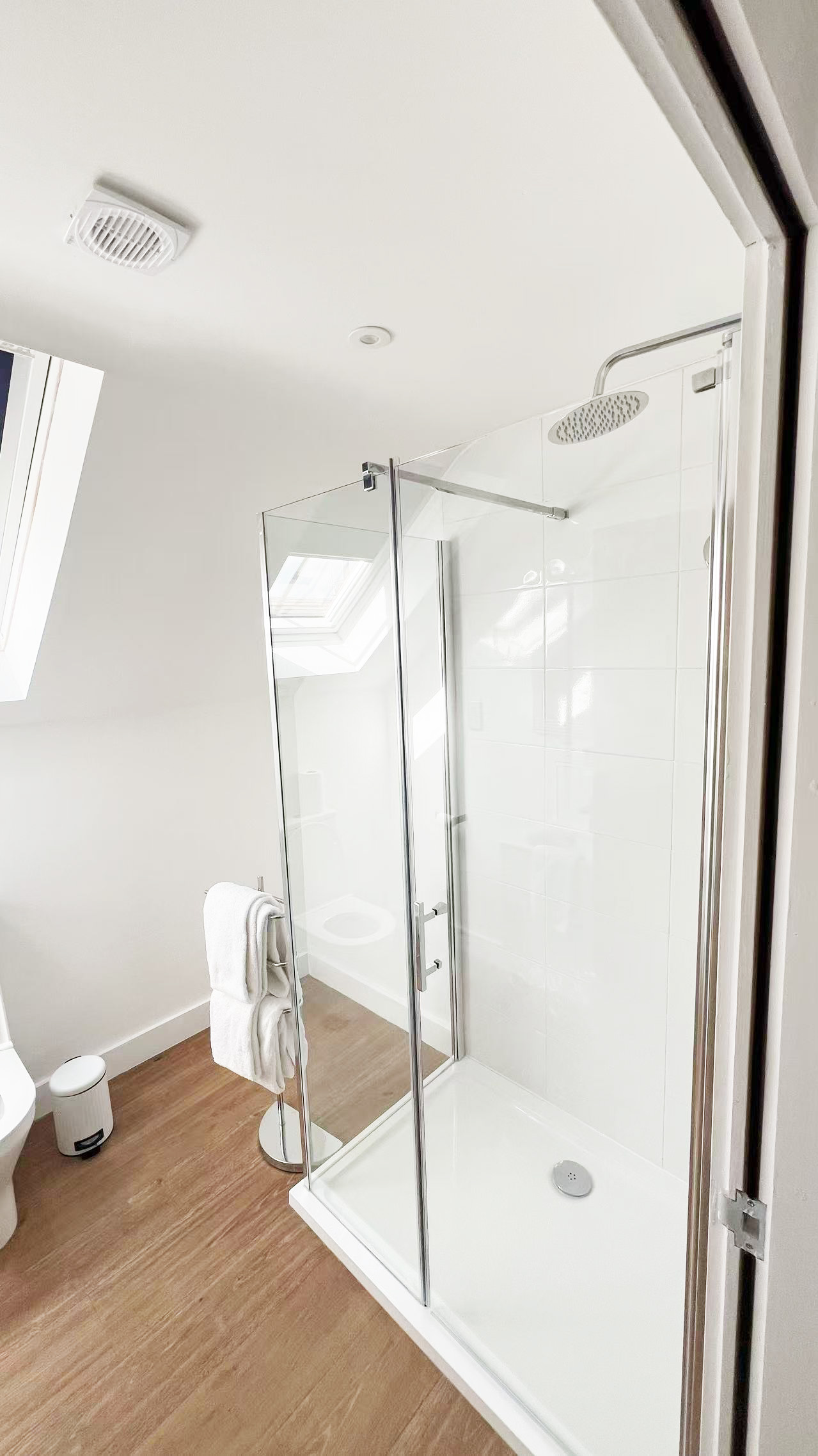 Modern bathroom with a glass shower enclosure, rainfall showerhead, white tile walls, and wood-look flooring