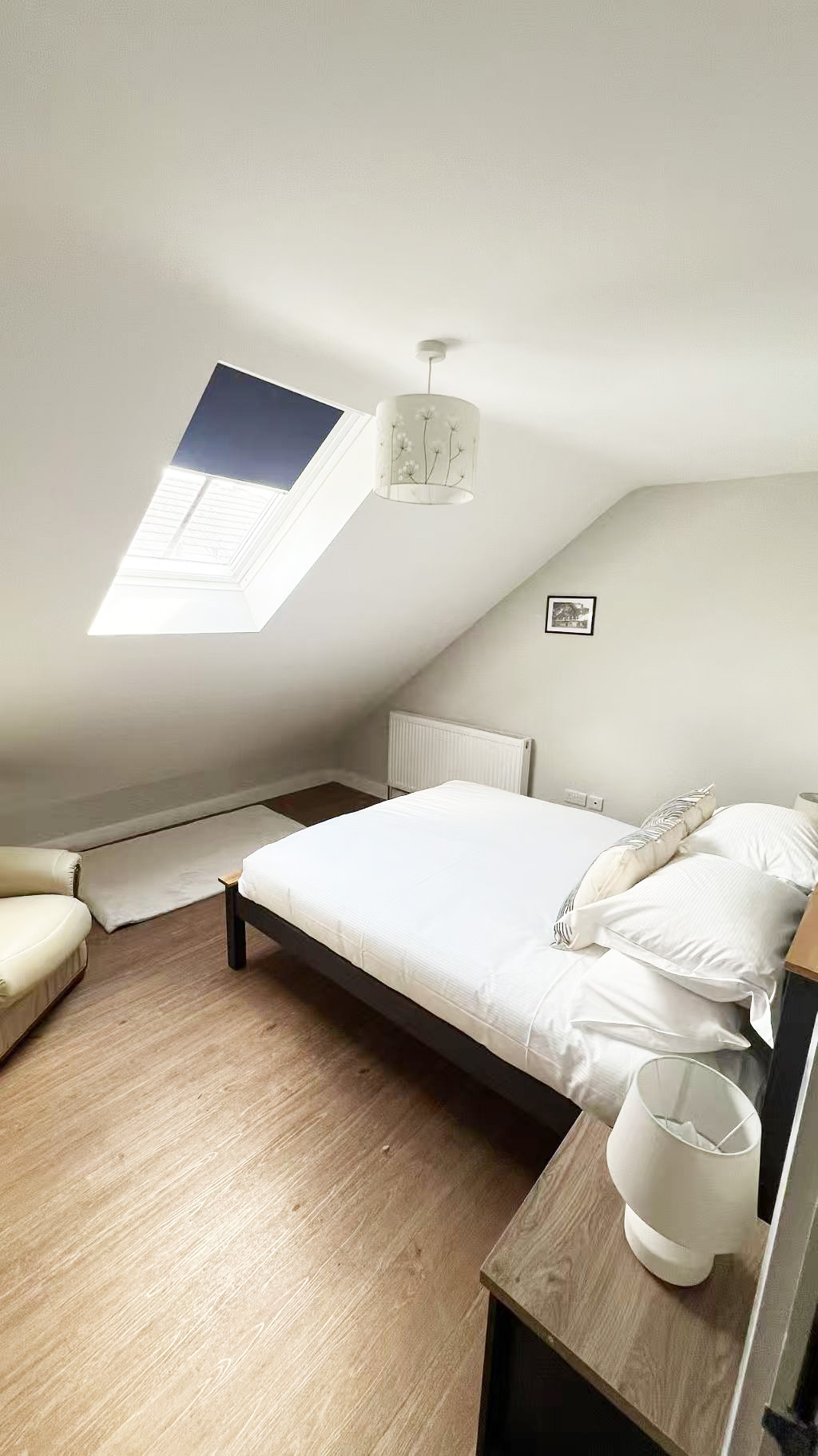 Bedroom with a sloped ceiling, skylight window, and a neatly made bed with white linens.