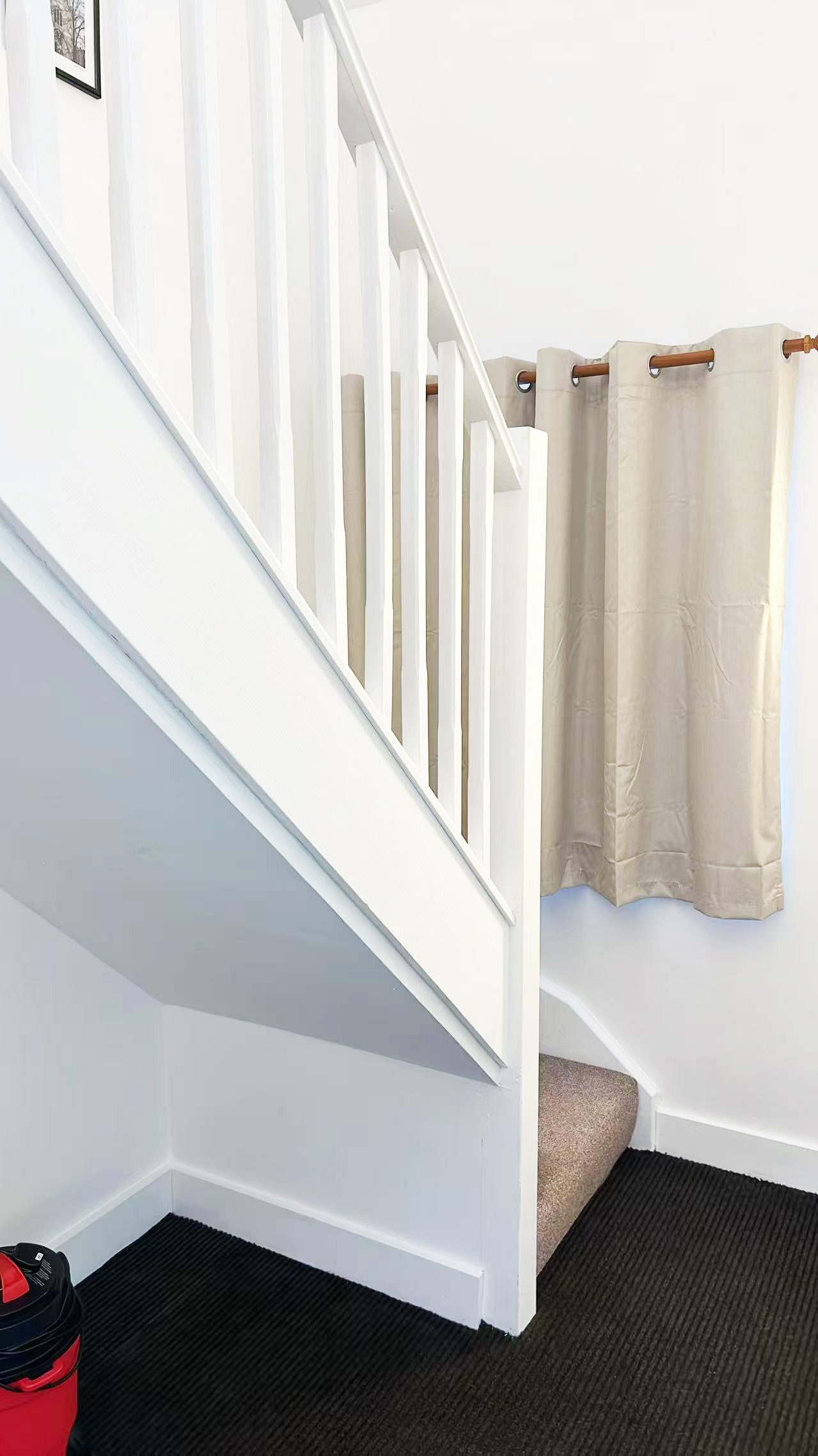 Interior staircase with white balustrade and beige curtains along the wall; dark ribbed carpet on the steps/landing.