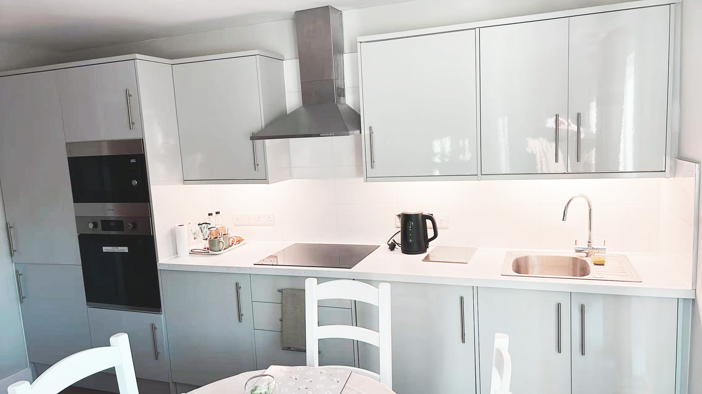 Modern grey kitchen with built-in oven, induction hob, and stainless steel range hood above a white counter.